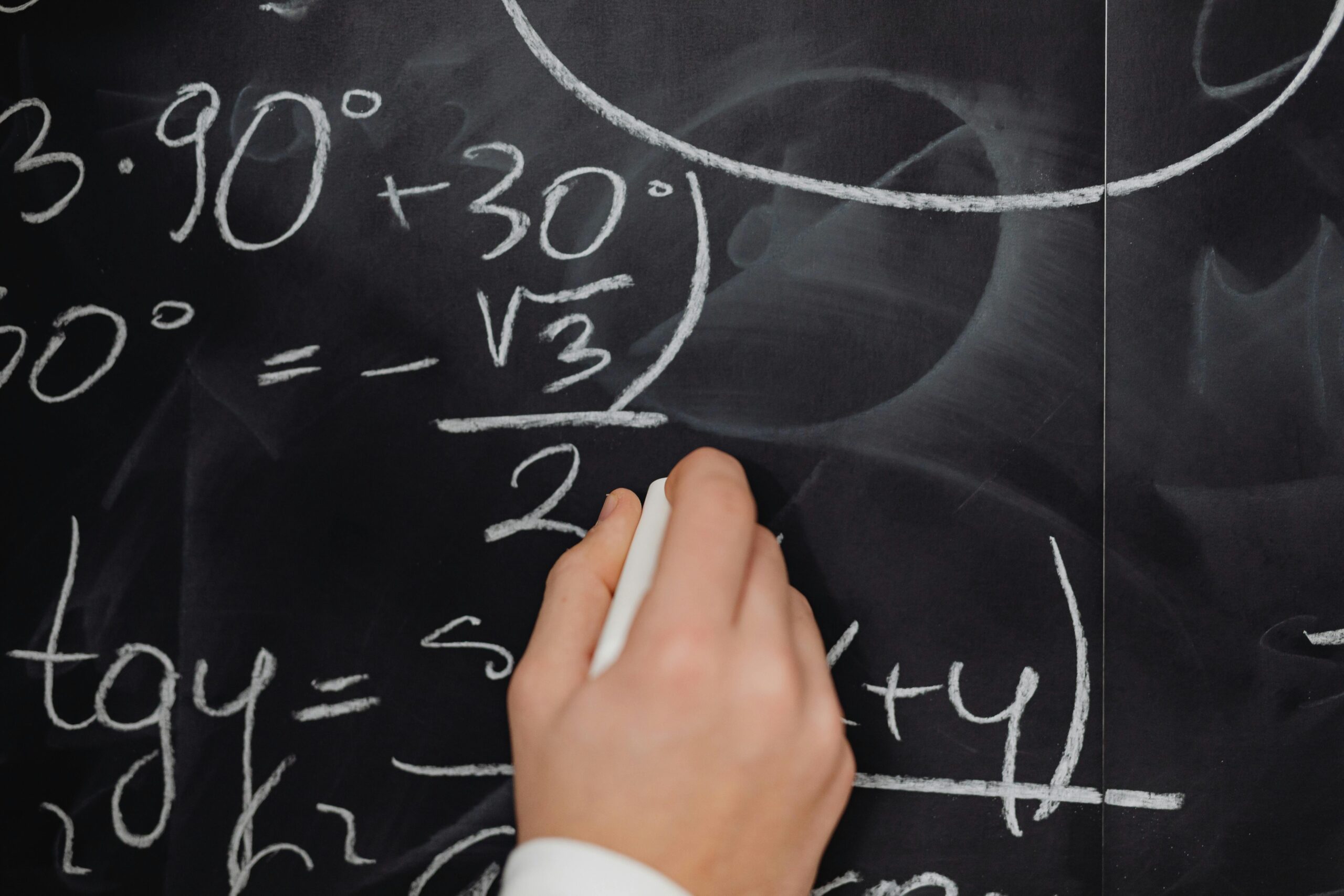 Academics A hand vividly writing complex mathematical equations on a chalkboard.